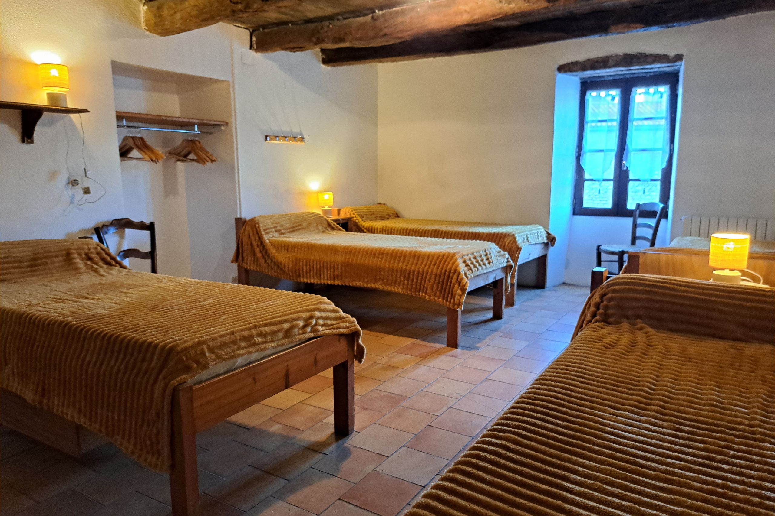 Chambre de 5 lits avec plusieurs lits sous poutres bois au 1er étage du gîte d’étape de la Tour du Viala‑du‑Pas‑de‑Jaux.
