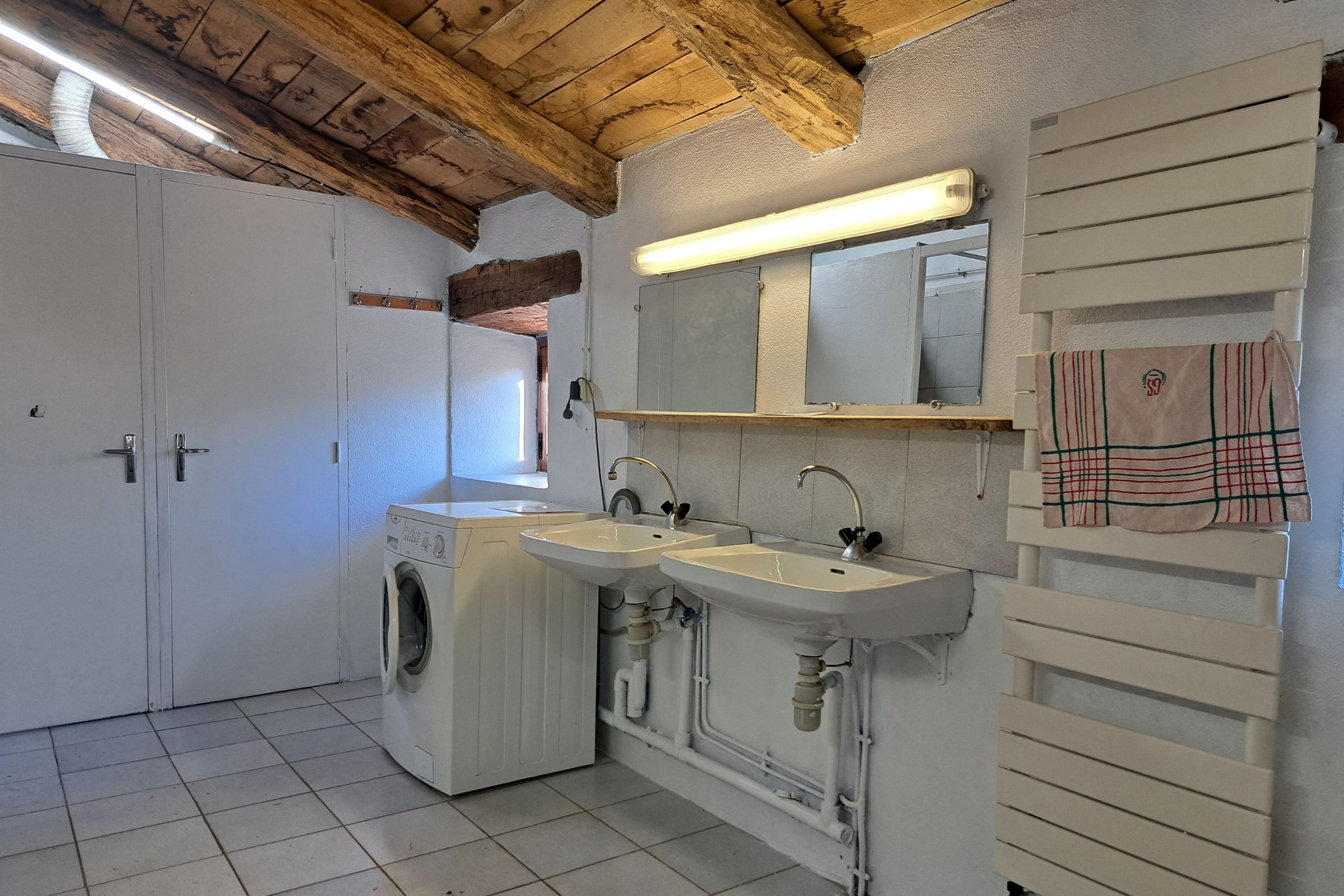 Salle de bain du gîte avec douches, lavabos, toilettes, machine à laver et poutres apparentes sous toiture.