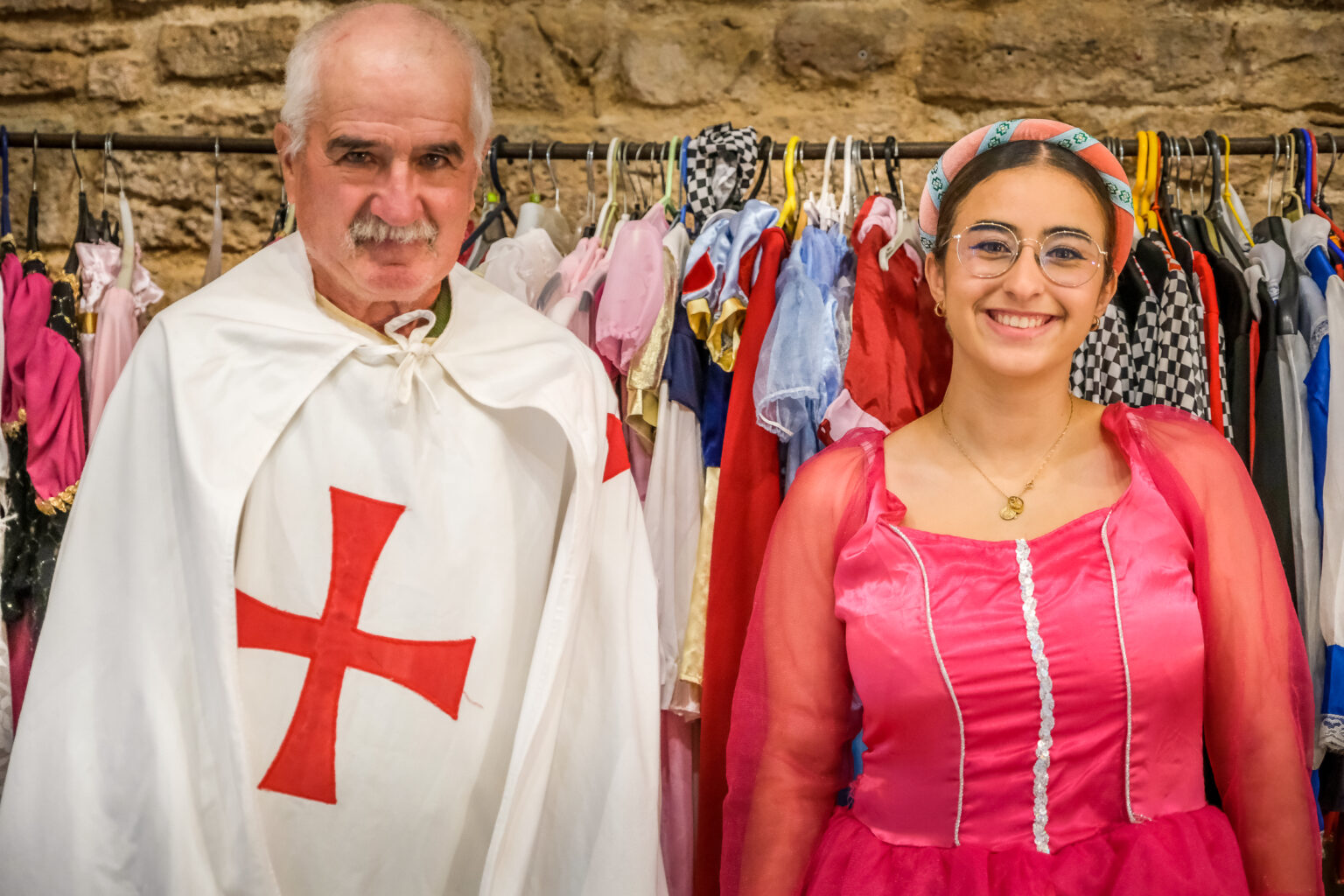 Deux personnes costumées en tenues médiévales devant un portant coloré à la Tour du Viala-du-Pas-de-Jaux.
