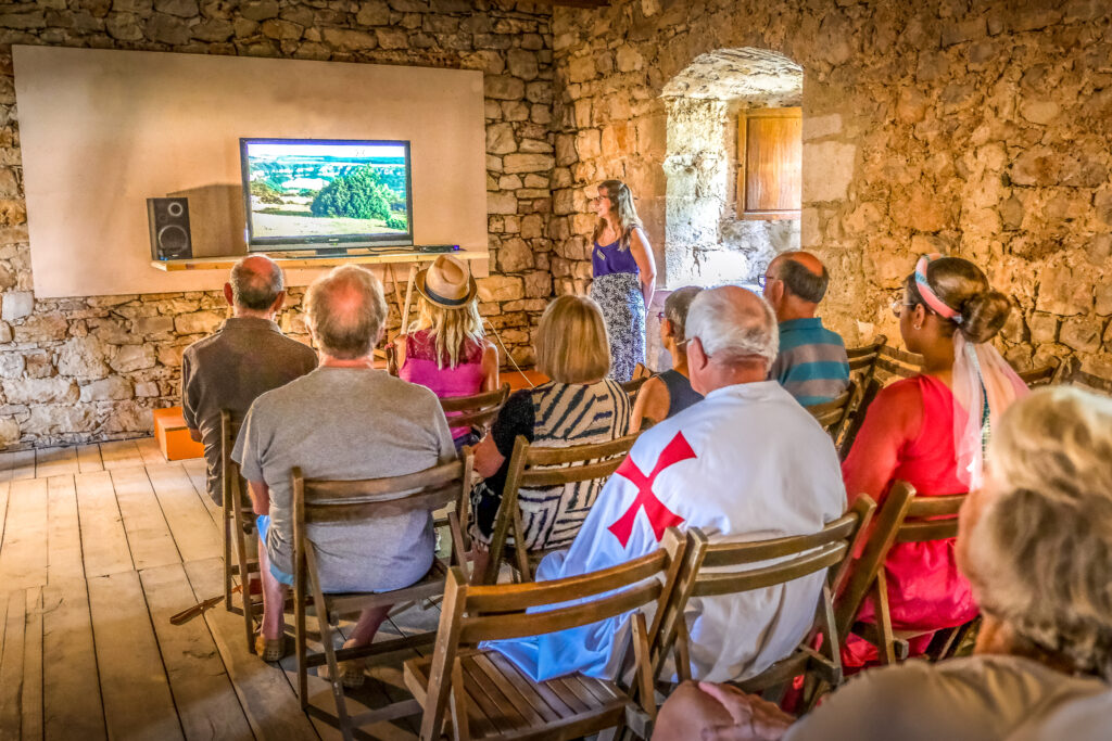 Visiteurs assistant à une projection vidéo sur l’histoire du Larzac et de la Tour du Viala du Pas de Jaux à l’intérieur du logis des templiers.