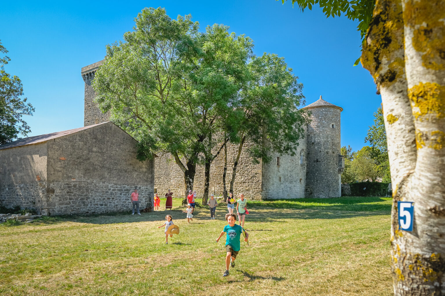 Enfants jouant sur l’esplanade verdoyante près de la Tour du Viala-du-Pas-de-Jaux sous un ciel bleu d’été.