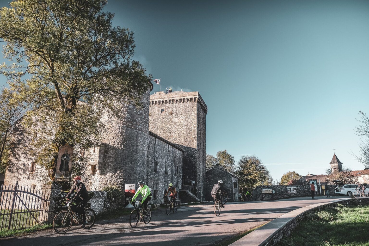 Cyclistes en gravel passant devant la Tour du Viala-du-Pas-de-Jaux, monument médiéval du Larzac.