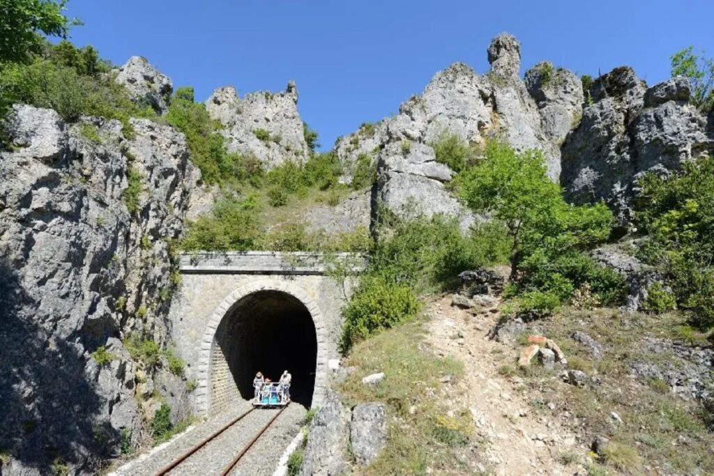 Groupe de visiteurs en vélorail sortant d’un tunnel creusé dans la roche sur l’ancienne voie ferrée du Larzac.
