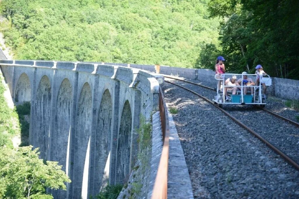 Famille en vélorail traversant un grand viaduc au-dessus de la vallée boisée de Ste Eulalie de Cernon.
