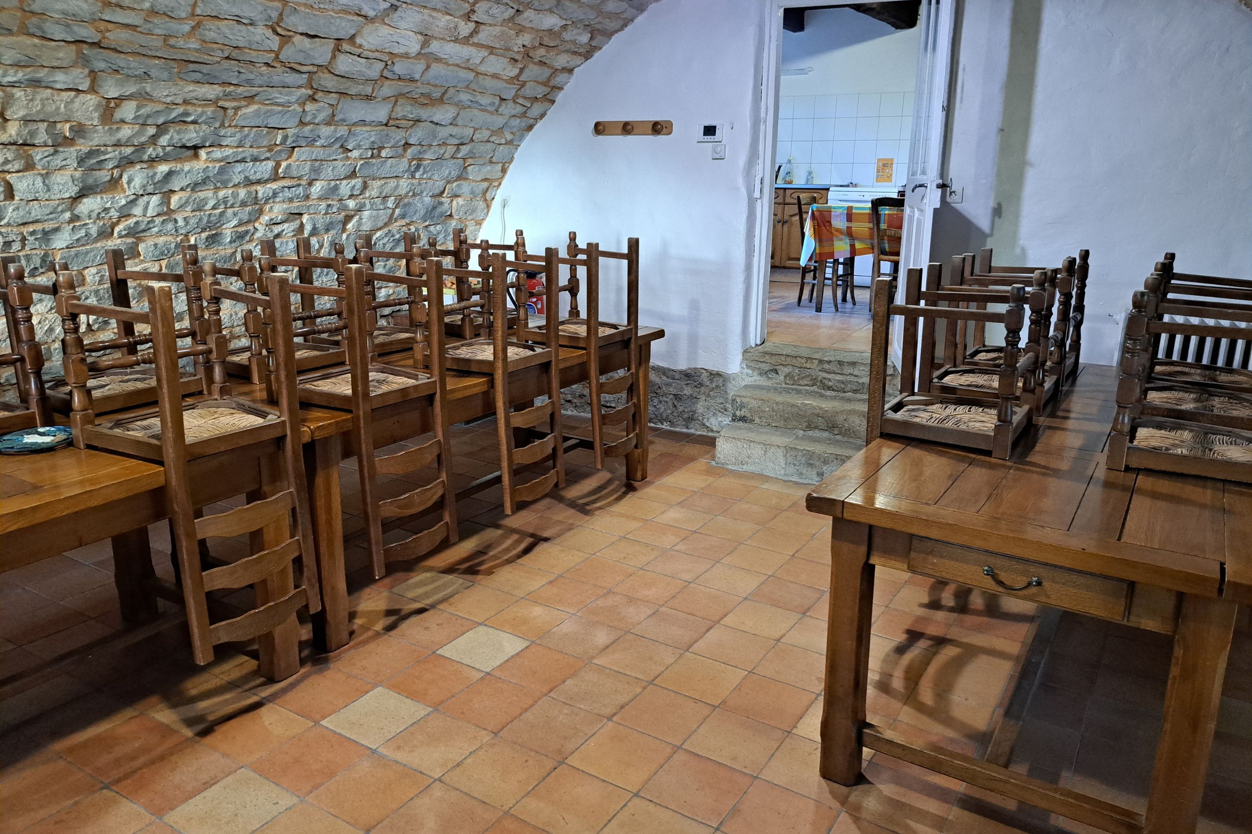 Salle à manger voûtée en pierre du gîte d’étape de la Tour du Viala‑du‑Pas‑de‑Jaux avec tables en bois et chaises empilées.
