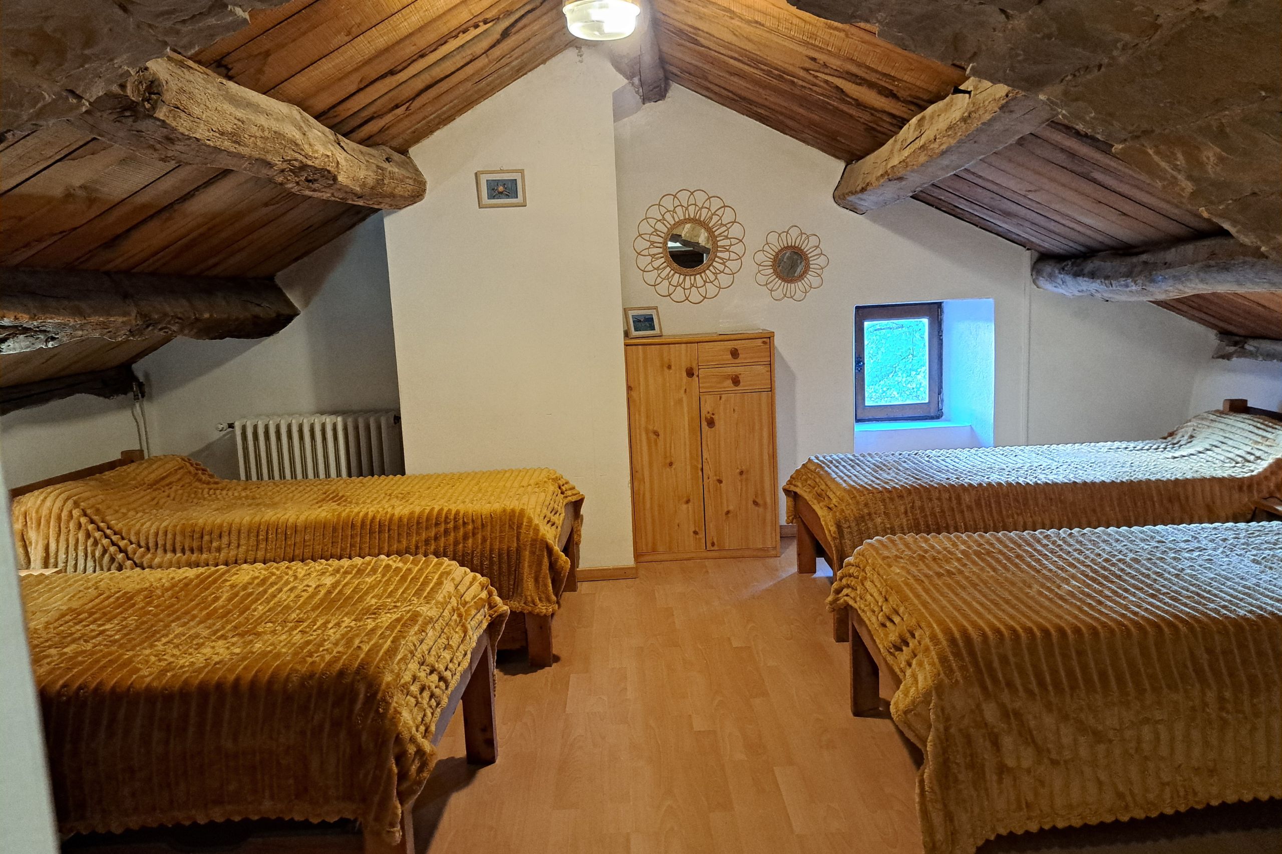 Chambre sous combles avec 4 lits simples alignés et couverture ocre au gîte d’étape de la Tour du Viala‑du‑Pas‑de‑Jaux.